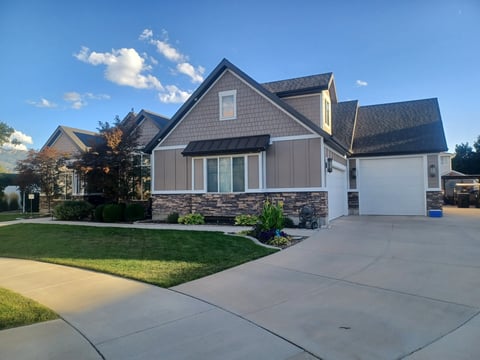 Modern two-story residential home with gray and white exterior, stone accents, attached garage, manicured lawn, and concrete driveway under clear blue sky