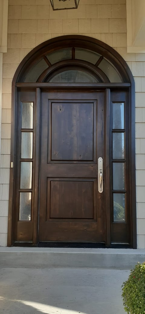 Dark wood arched front door with glass sidelights and transom window on beige shingle house