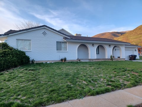 Single-story white ranch house with arched portico entrance and green lawn, set against hillside backdrop