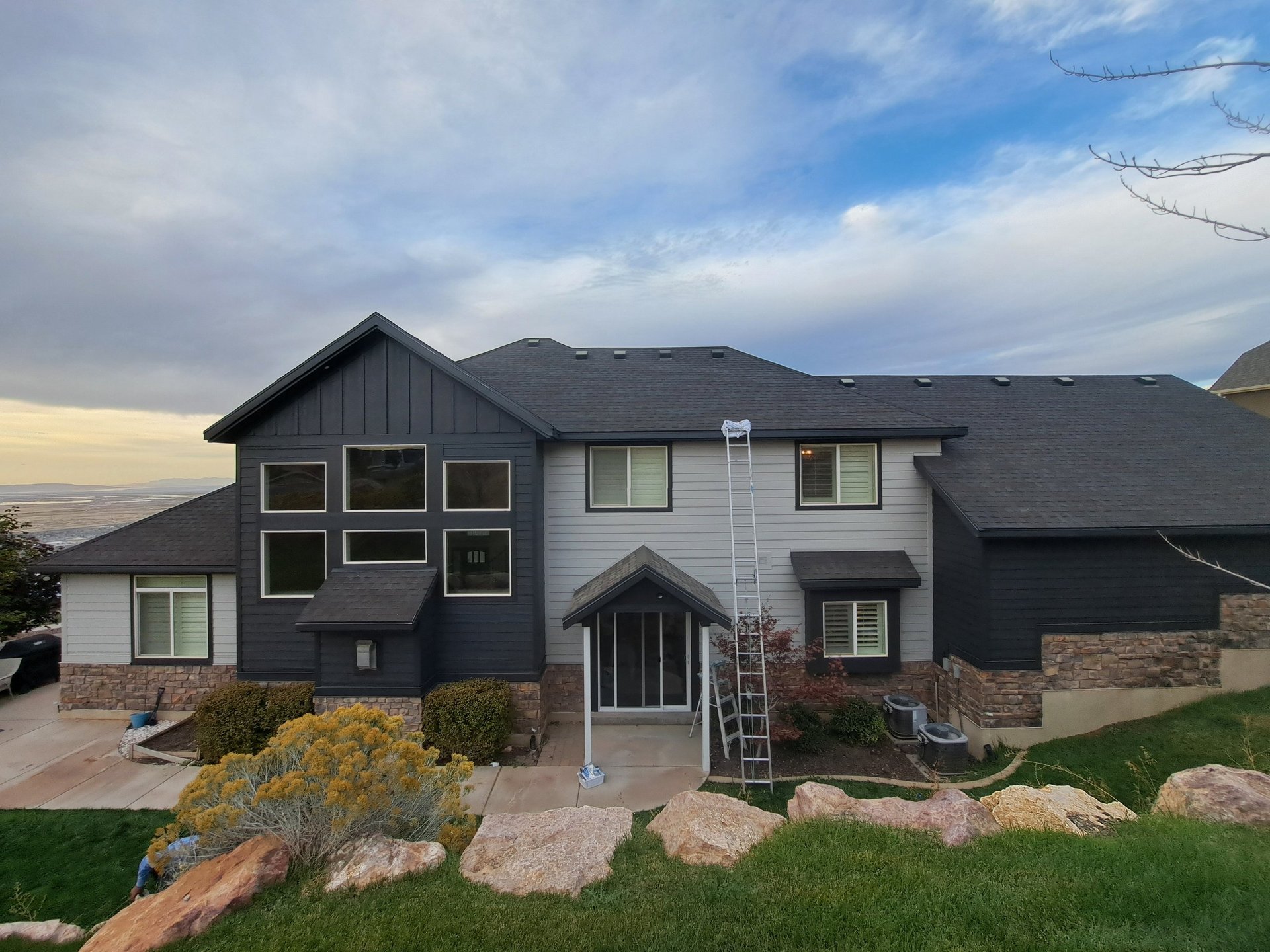Modern two-story home with dark exterior, stone accents, and manicured landscaping against a scenic hillside backdrop