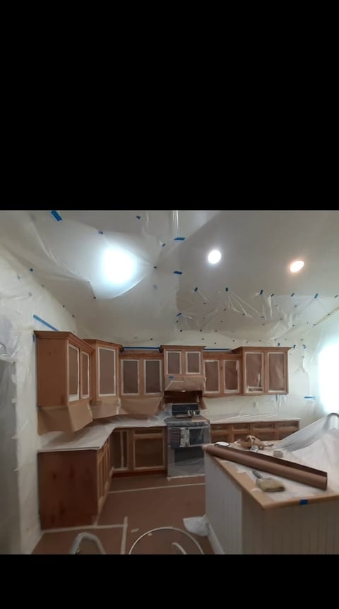 Kitchen under renovation with wooden cabinets, exposed ceiling, LED lights, and construction materials scattered throughout